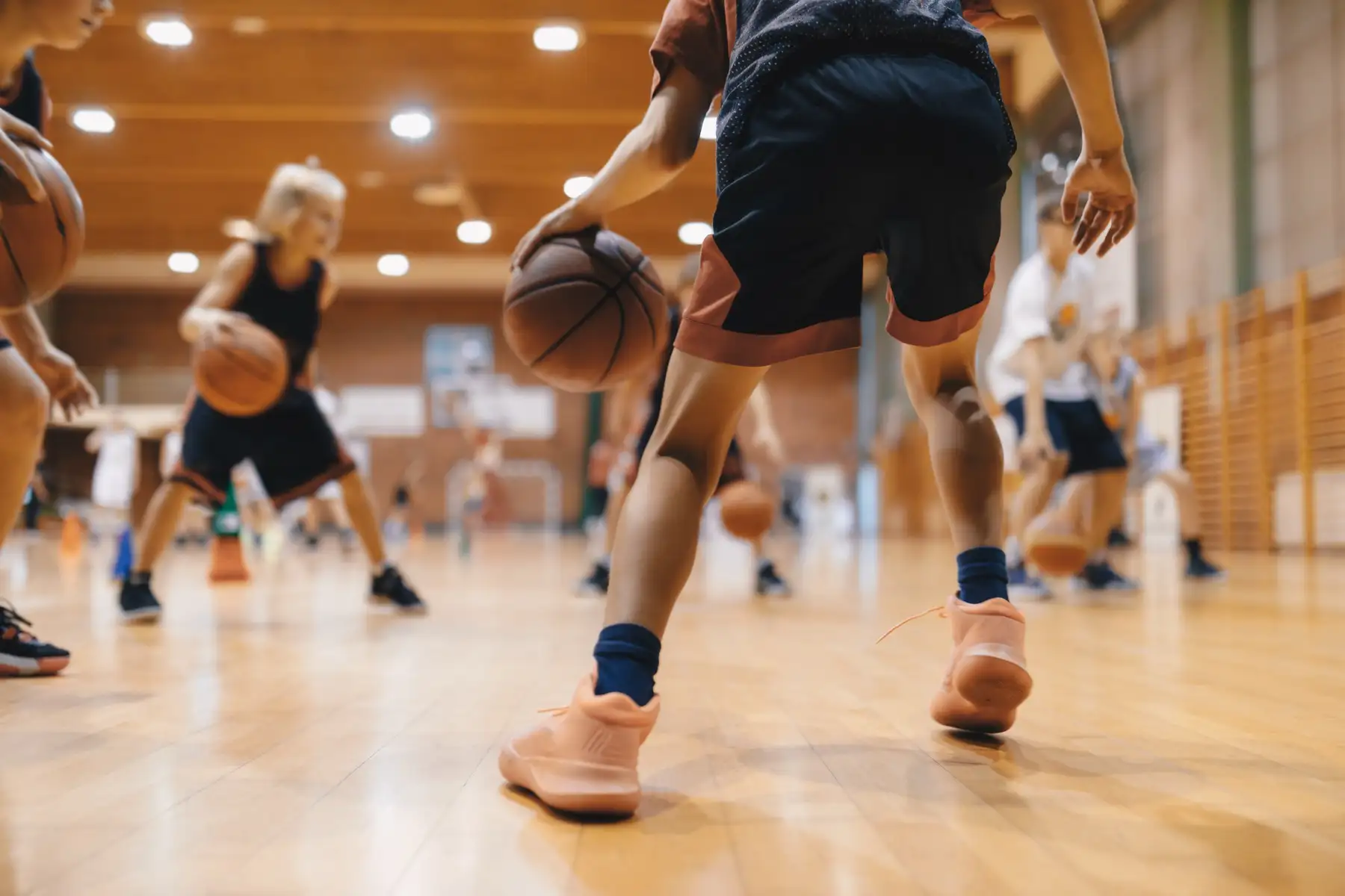 Young players dribbling basketballs during a practice in a school gym