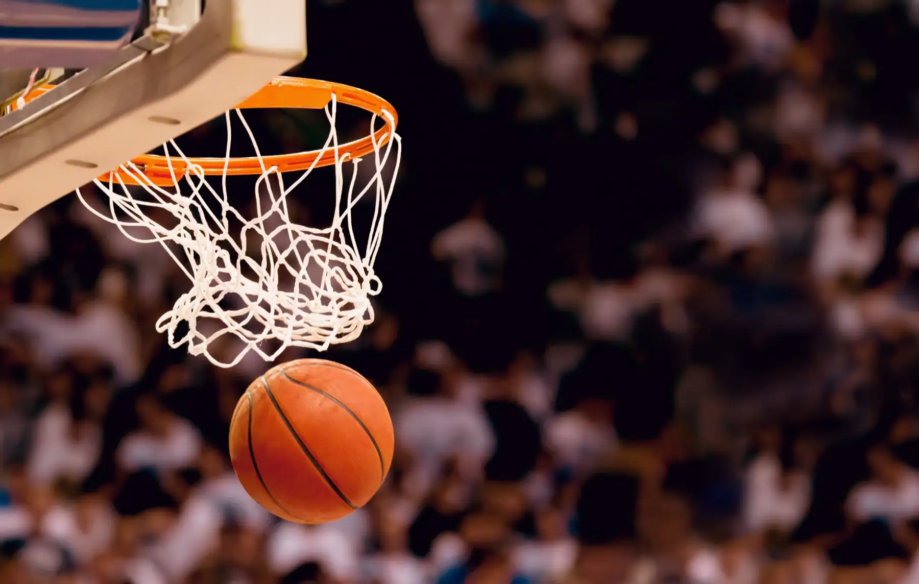 A basketball dropping through the net in front of a packed crowd
